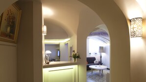 A hallway with patterned floor tiles, an arched doorway, a reception desk, a sofa, and a lamp. - Louis Appartements Galata (Istanbul)