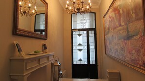 A hallway with a chandelier, a large mirror, a painting, and a door with frosted glass panels. - Louis Appartements Galata (Istanbul)