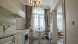 A compact kitchen with modern appliances, a dining area with a table and chairs, and a view of the living room through an open door. - Louis Appartements Galata (Istanbul)