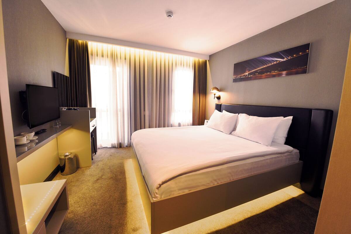 A hotel room with a large bed, a television, a desk with a computer, and a painting on the wall.