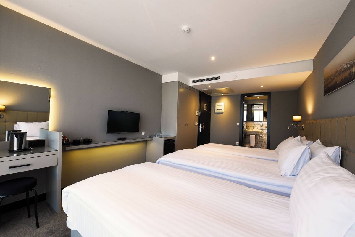 A hotel room with two beds, a desk with a television, and a bathroom visible through an open door.