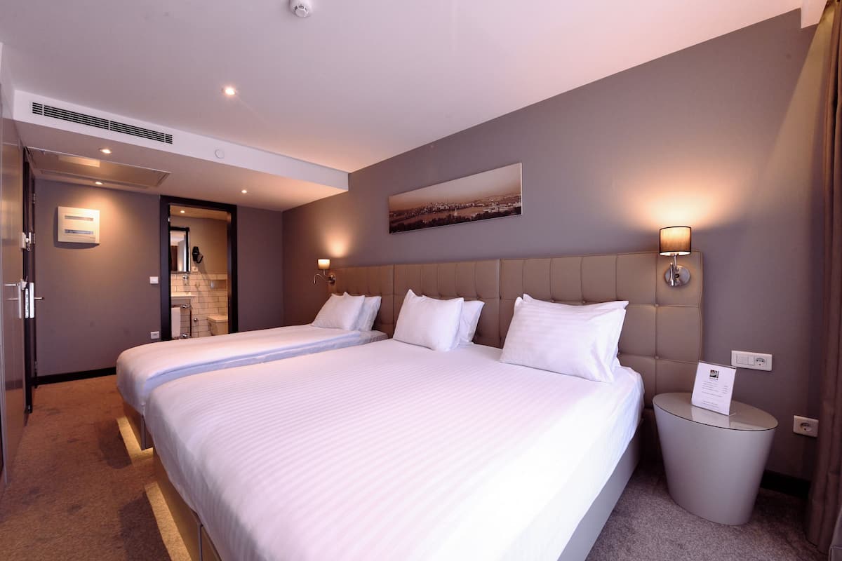 A hotel room with a large bed, a headboard, bedside lamps, a small bedside table, and a picture on the wall.