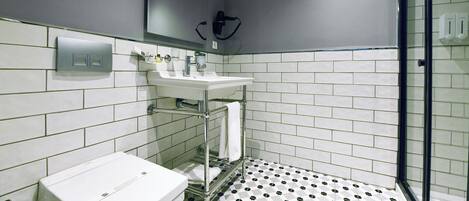 A bathroom with a white sink, mirror, and toilet, tiled floor with a black and white pattern, and a glass shower enclosure.