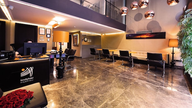 Un espace d’accueil d’hôtel au design moderne, comprenant un comptoir d’accueil, un coin salon et une grande fenêtre donnant sur l’intérieur.
