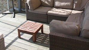 Un espacio al aire libre con techo, mobiliario de mimbre que incluye un sofá y una mesa de madera, pared de ladrillo.
