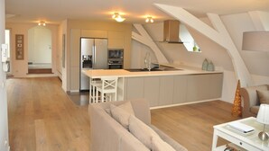 Una cocina moderna con una isla central, un rincón de comedor con sofá y una escalera que sube a un nivel superior.