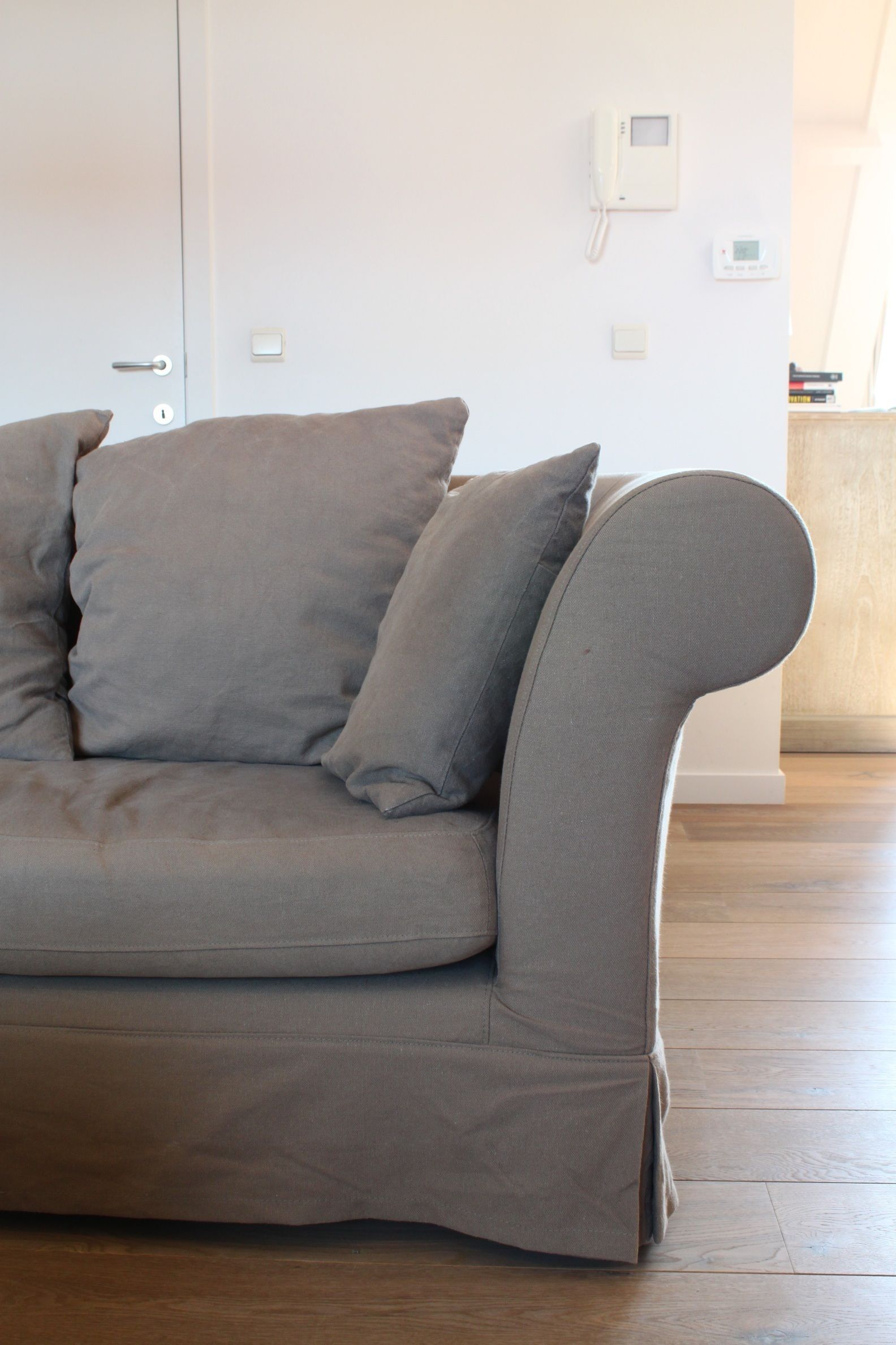 A grey sofa with a curved backrest in a room with wooden flooring and white walls.