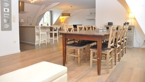 Un comedor con una mesa y sillas de madera, una cocina al fondo y un techo inclinado.