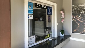 Uma área de recepção de escritório com uma placa indicando ser um escritório e que cães de serviço são permitidos. Há uma planta em vaso no balcão e uma fotografia emoldurada de um horizonte urbano na parede.