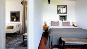 Un dormitorio con cama, mesitas de noche, sillón, sofá y un jarrón decorativo.