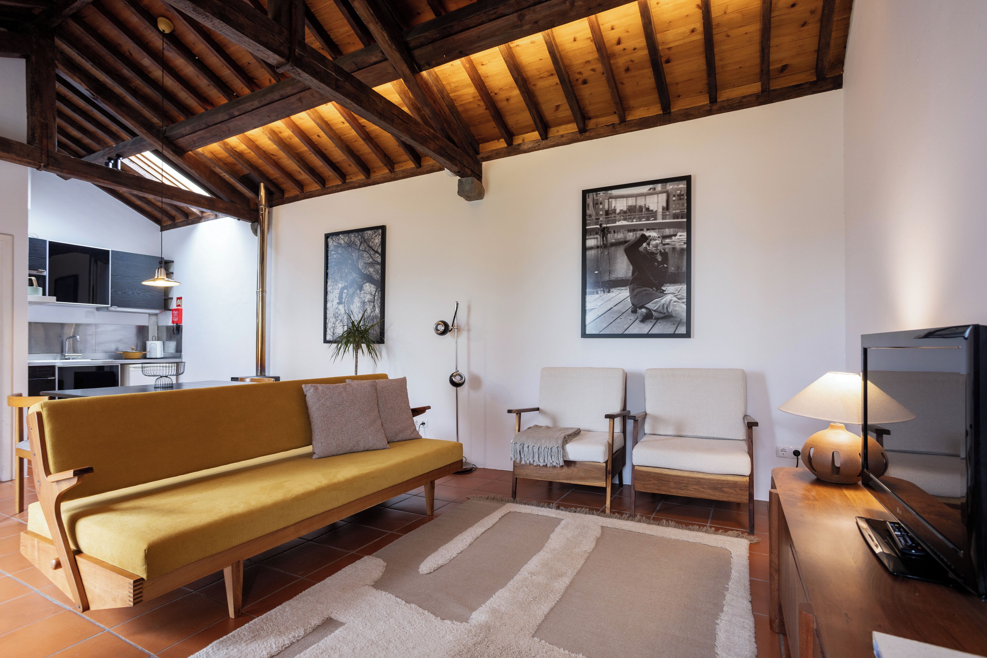 Una sala de estar con techo de madera, un sofá, un sillón, un televisor y una lámpara.