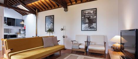 Una sala de estar con techo de madera, un sofá, un sillón, un televisor y una lámpara.