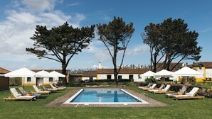 Una piscina con sillones de descanso y sombrillas, rodeada de árboles y edificios.
