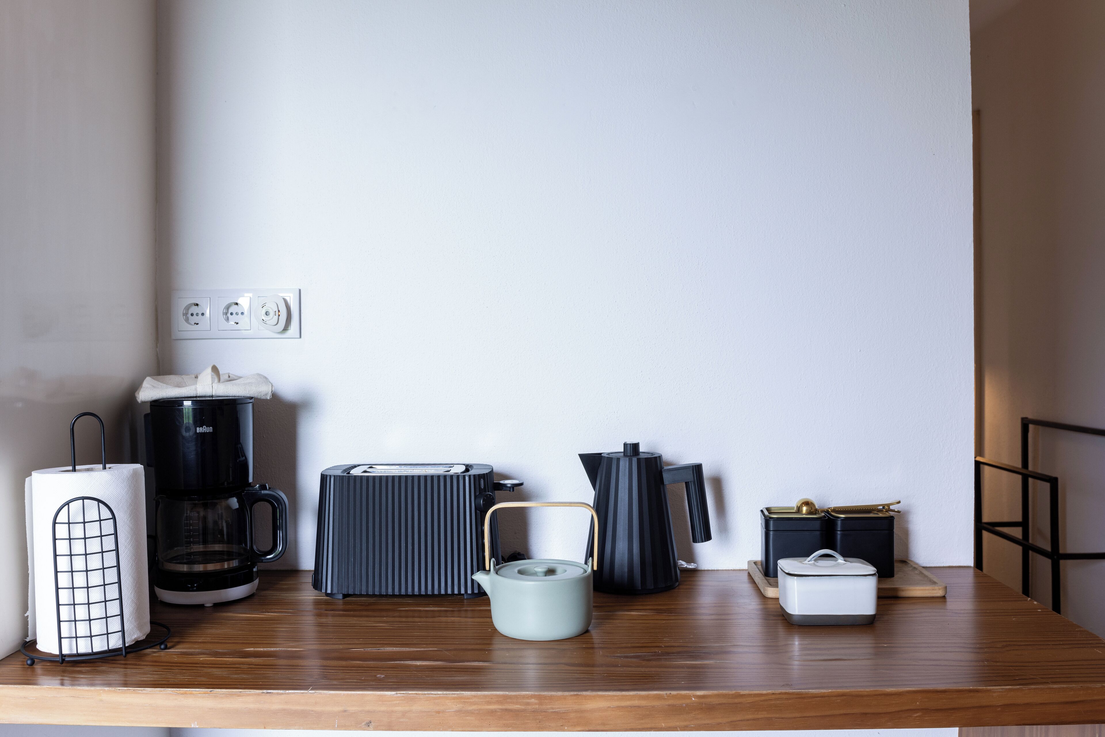 A kitchen counter with a coffee maker, kettle, toaster, and a kettle with a handle.