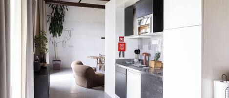 A modern kitchen with a built-in oven, a dining area with a sofa, and a plant.