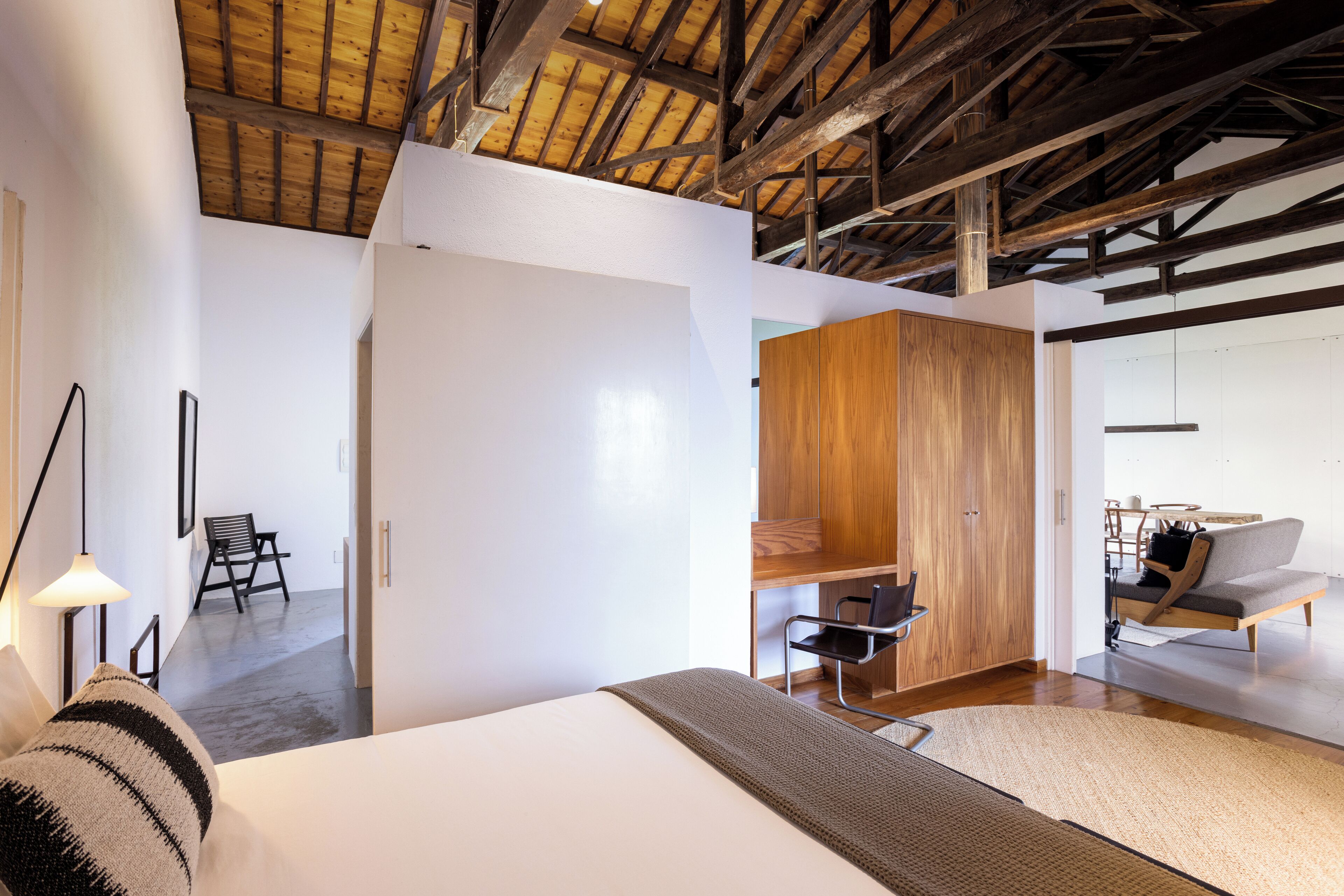 A modern hotel room with a large bed, wooden ceiling beams, a desk, and a sofa.