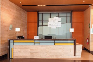 A reception desk with a Holiday Inn sign, a fire extinguisher, and a glass partition.