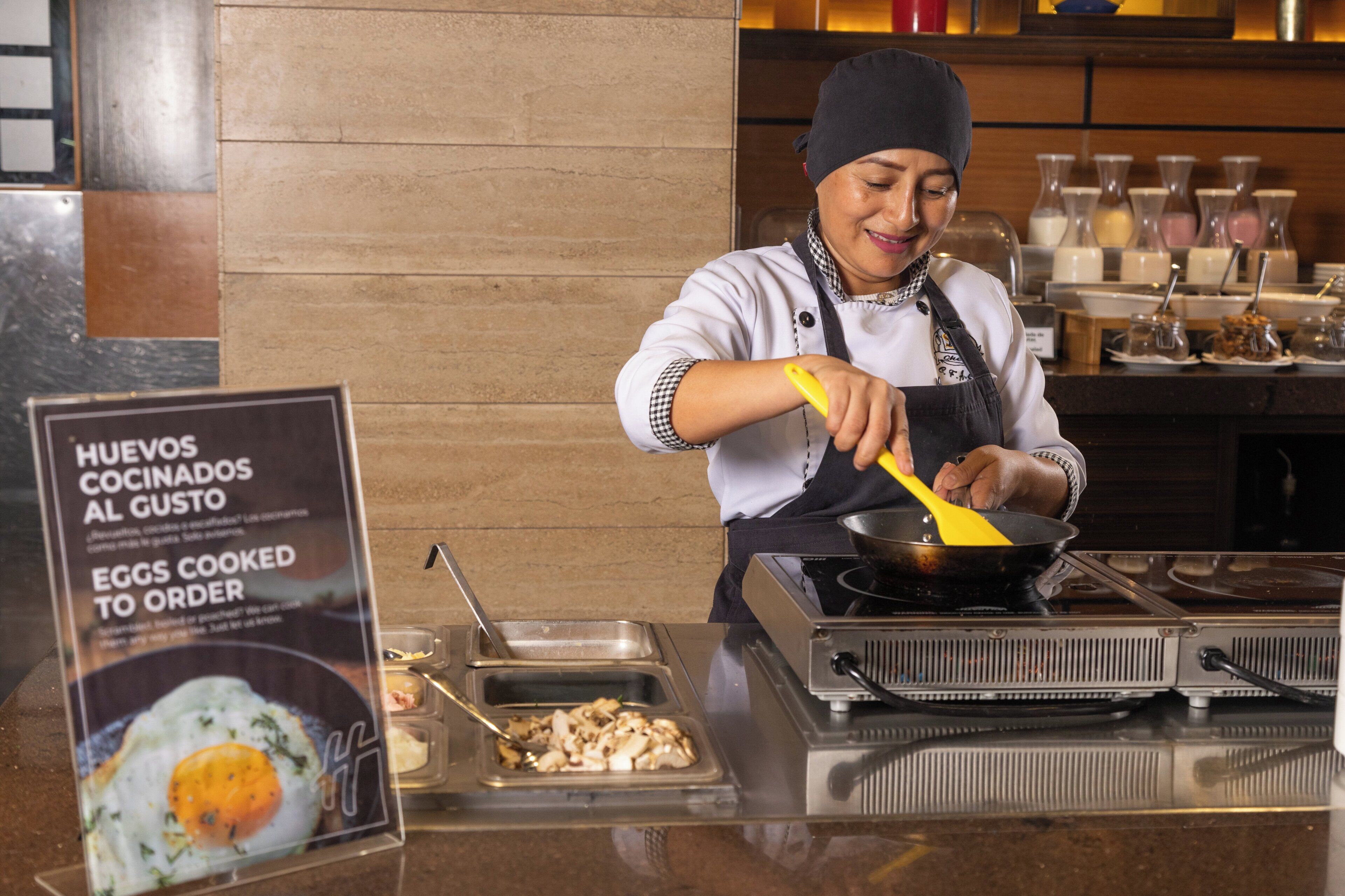 A person cooking eggs in a pan at a food station with a sign indicating eggs cooked to order.
