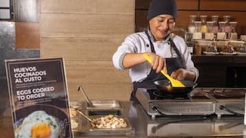 A person cooking eggs in a pan at a food station with a sign indicating eggs cooked to order.