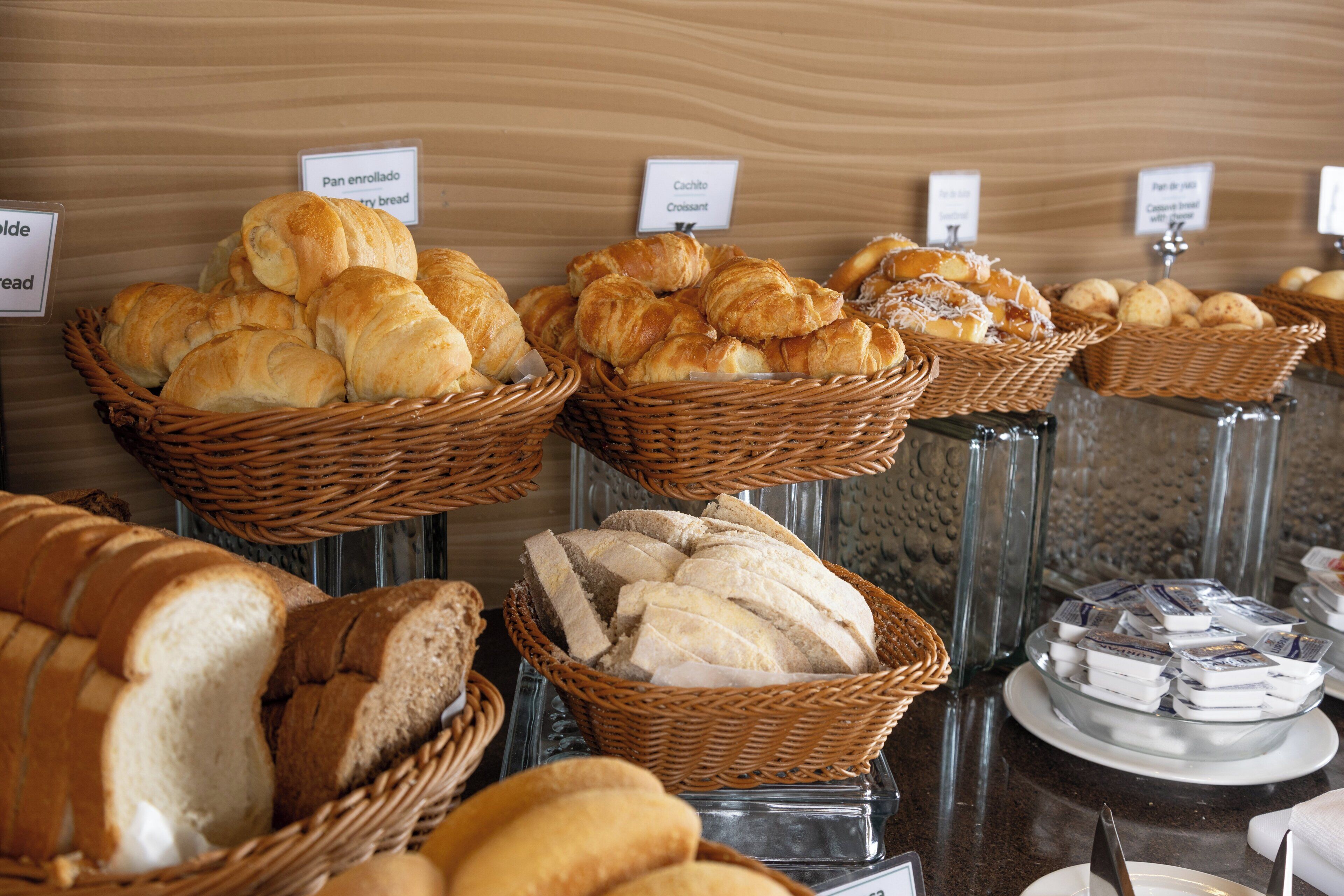 Verschiedene Brotsorten und Gebäckstücke in Körben und auf einer Theke, mit Schildern, die die jeweiligen Sorten kennzeichnen.