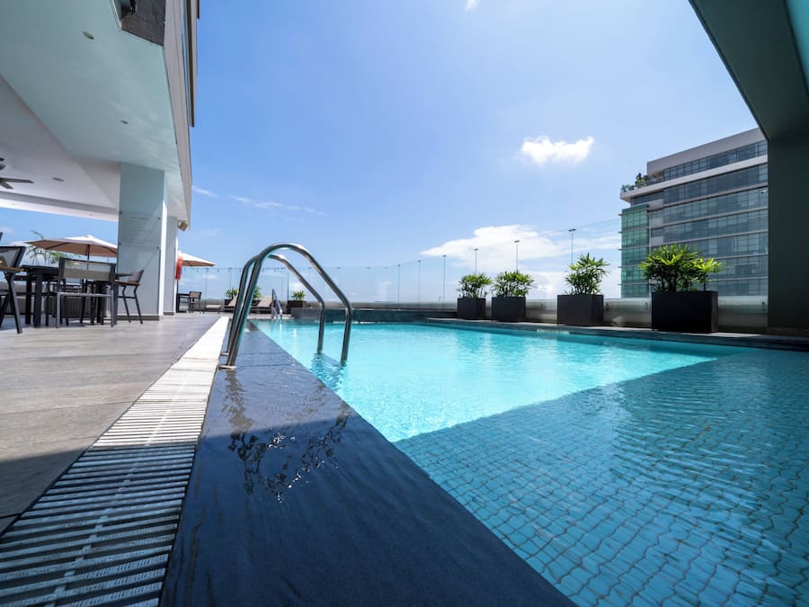 A rooftop pool with a clear view of the city skyline, surrounded by outdoor seating and potted plants.
