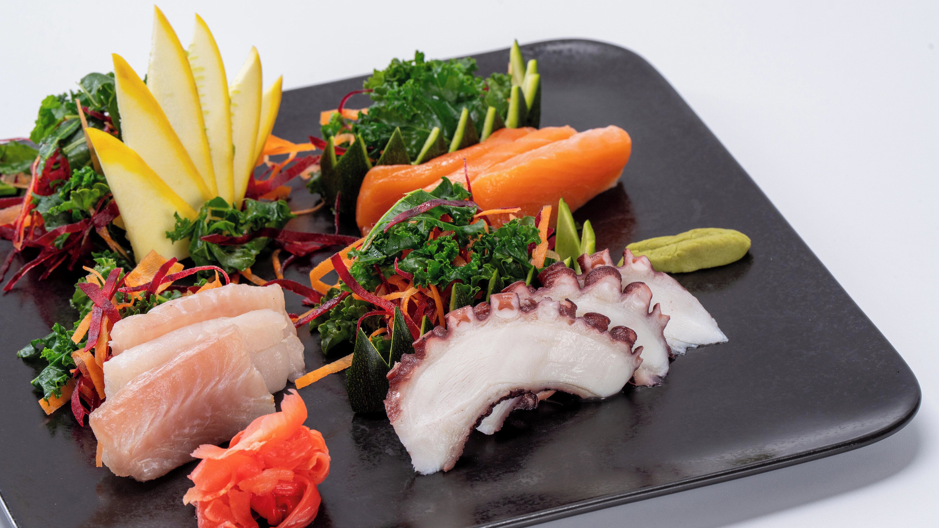 Un plato negro con diversos alimentos, incluyendo pulpo, pescado y verduras.
