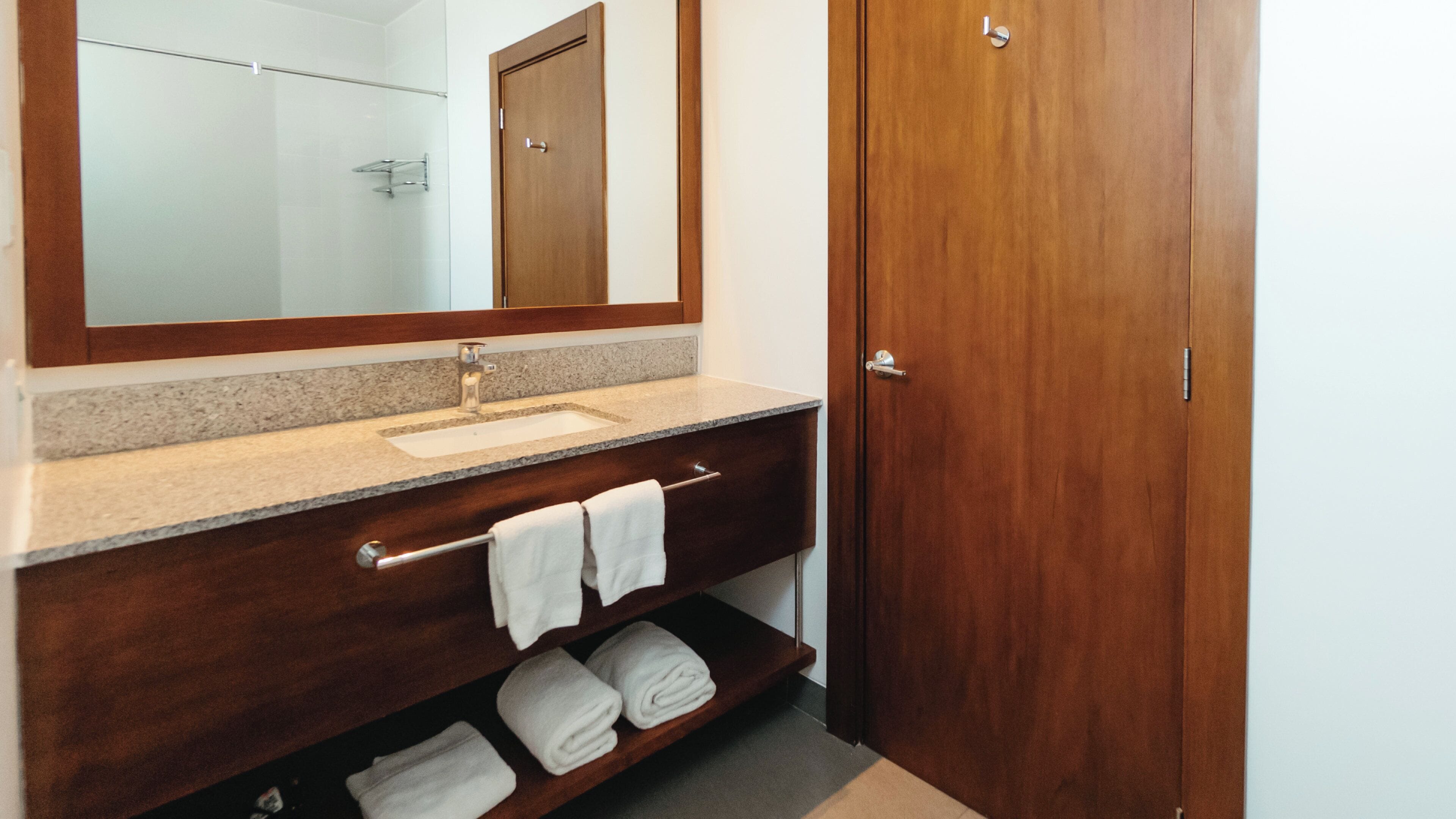 Un baño con tocador de madera, lavamanos, espejo y toallero.