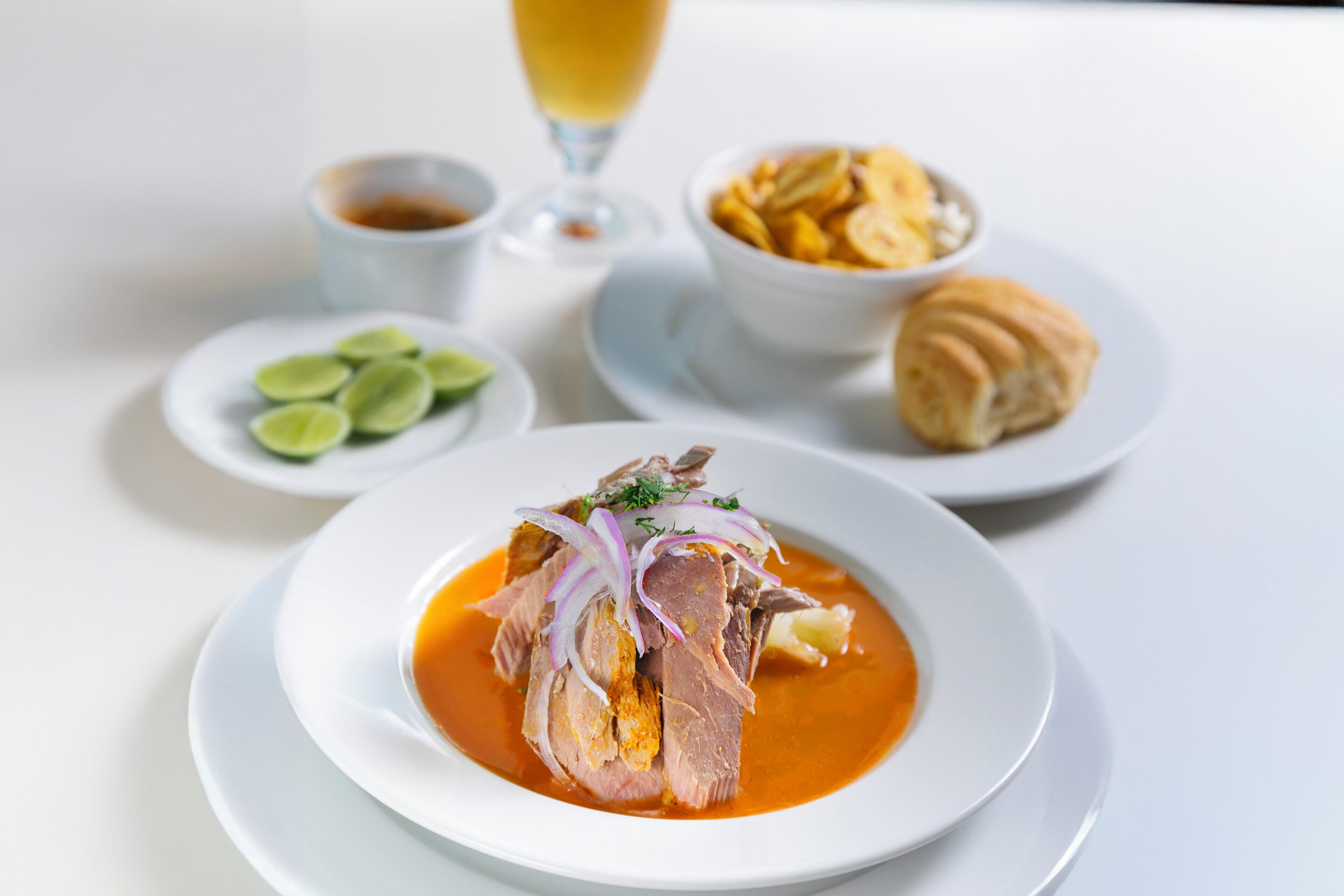 A plate of food with a glass of drink and a bowl of chips on a table.