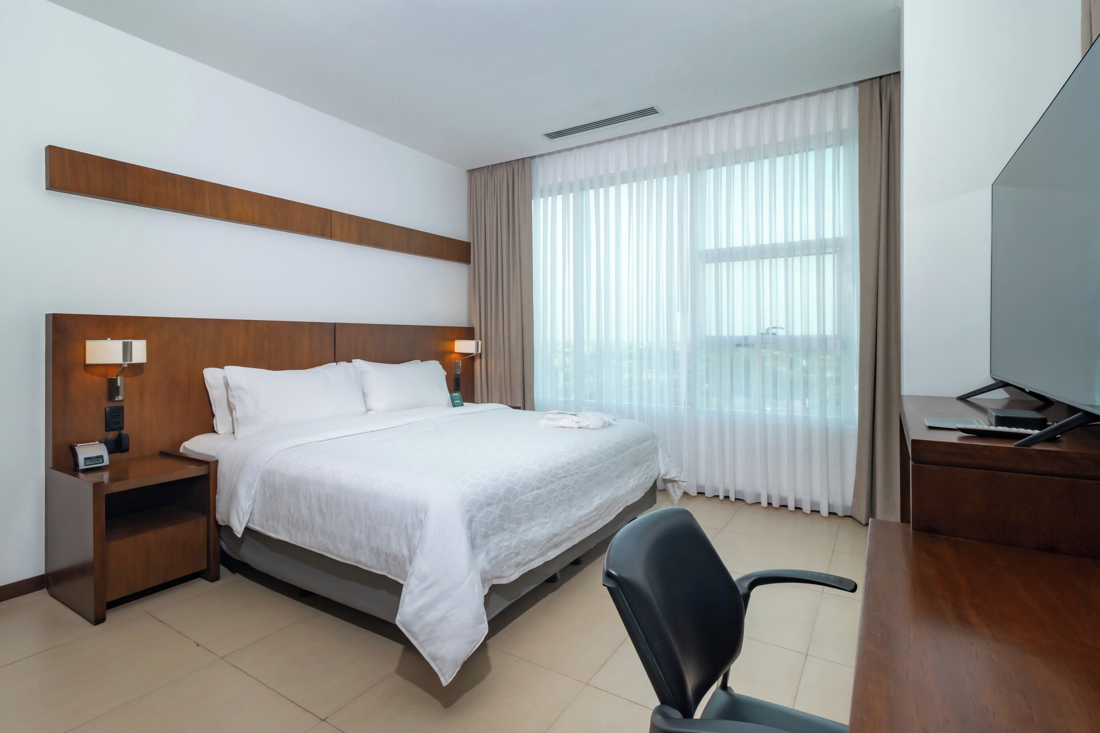 Habitación de hotel con una cama grande, mesitas de noche con lámparas, un escritorio con computadora y una silla.