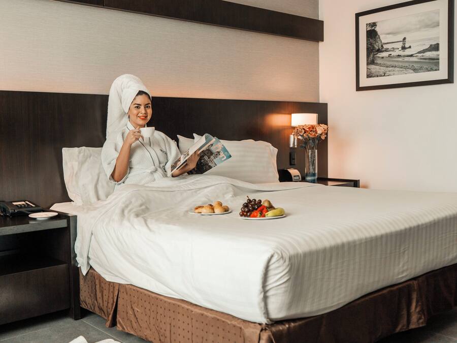 Une chambre d’hôtel avec un lit, une table de chevet, une petite table de nuit avec une lampe, et un tableau encadré au mur.