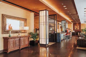 A hotel lobby with a reception desk, a large mirror, a potted plant, and a seating area with a sofa and chairs. - Holiday Inn Guayaquil Airport by IHG (Guayaquil)