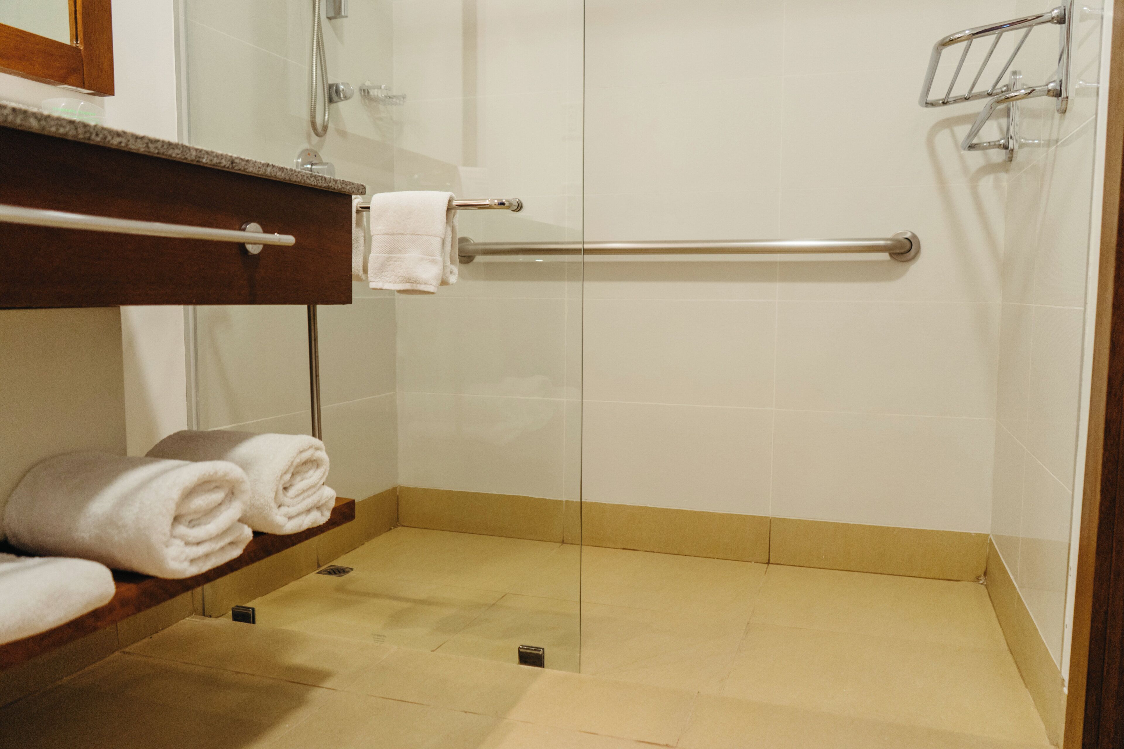 Un baño con mampara de vidrio, toallero y repisa con toallas dobladas.