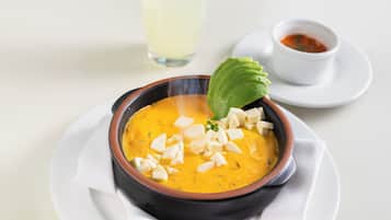 Un tazón de sopa con adornos, un recipiente pequeño con salsa y un vaso de líquido transparente sobre un plato blanco.