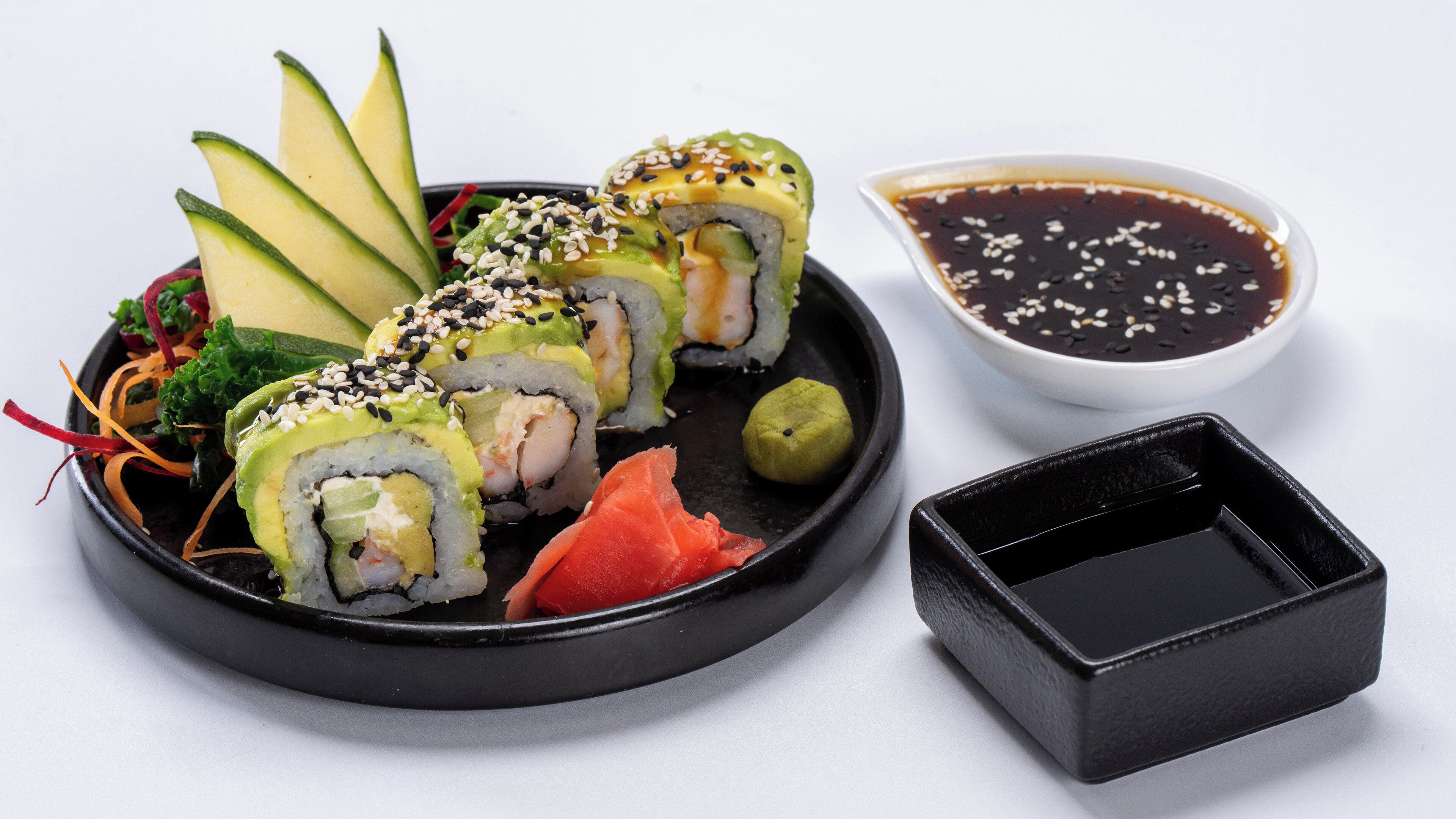 Une assiette de sushis à l’avocat, au saumon et aux graines de sésame, accompagnée d’un petit bol de sauce soja.