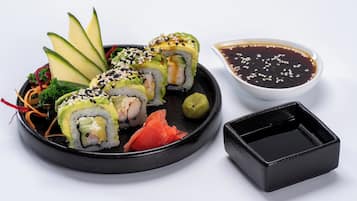 Une assiette de sushis à l’avocat, au saumon et aux graines de sésame, accompagnée d’un petit bol de sauce soja.