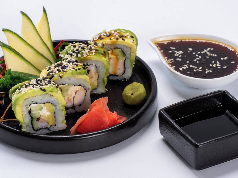 Une assiette de sushis à l’avocat, au saumon et aux graines de sésame, accompagnée d’un petit bol de sauce soja.