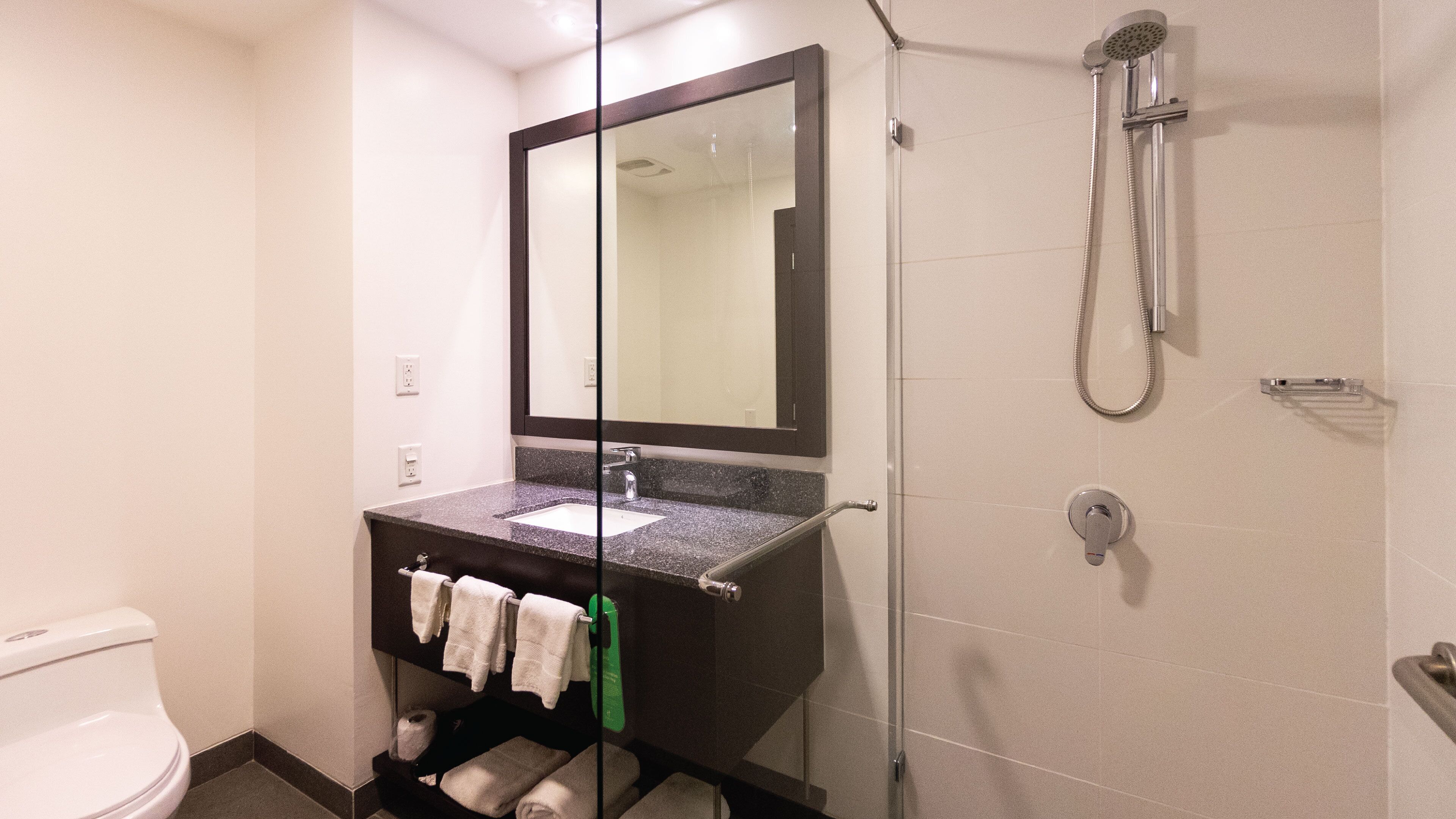 Een moderne badkamer met een douche in een glazen cabine, een grote spiegel en een wastafel met een granieten blad.