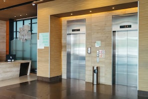 A modern elevator area with a reception desk, a digital display, and a trash bin.