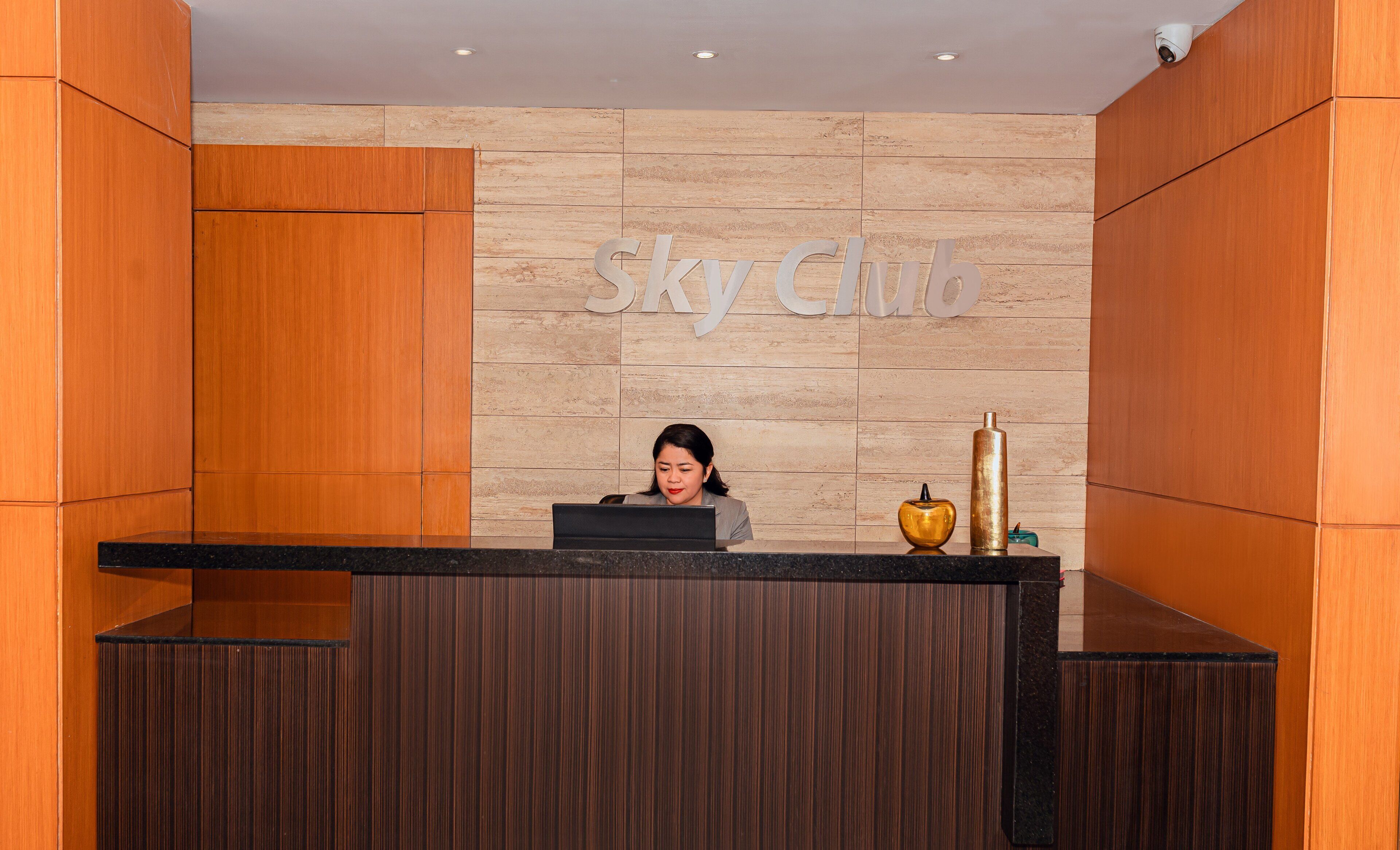 A reception desk with a 'Sky Club' sign, a receptionist, and a decorative vase.