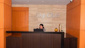 A reception desk with a 'Sky Club' sign, a receptionist, and a decorative vase.