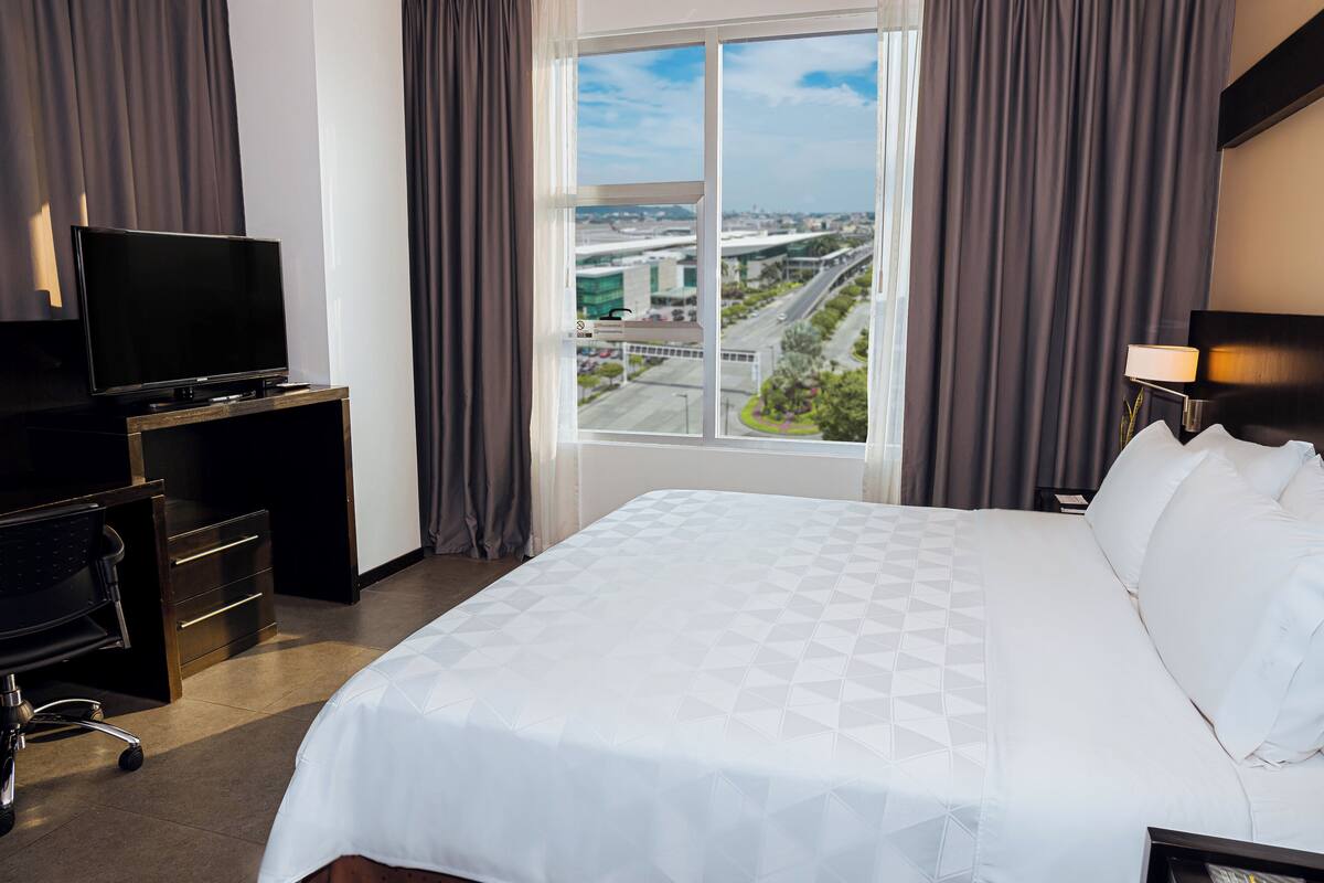 Een hotelkamer met een groot bed, een bureau met televisie en uitzicht op een stadsbeeld.