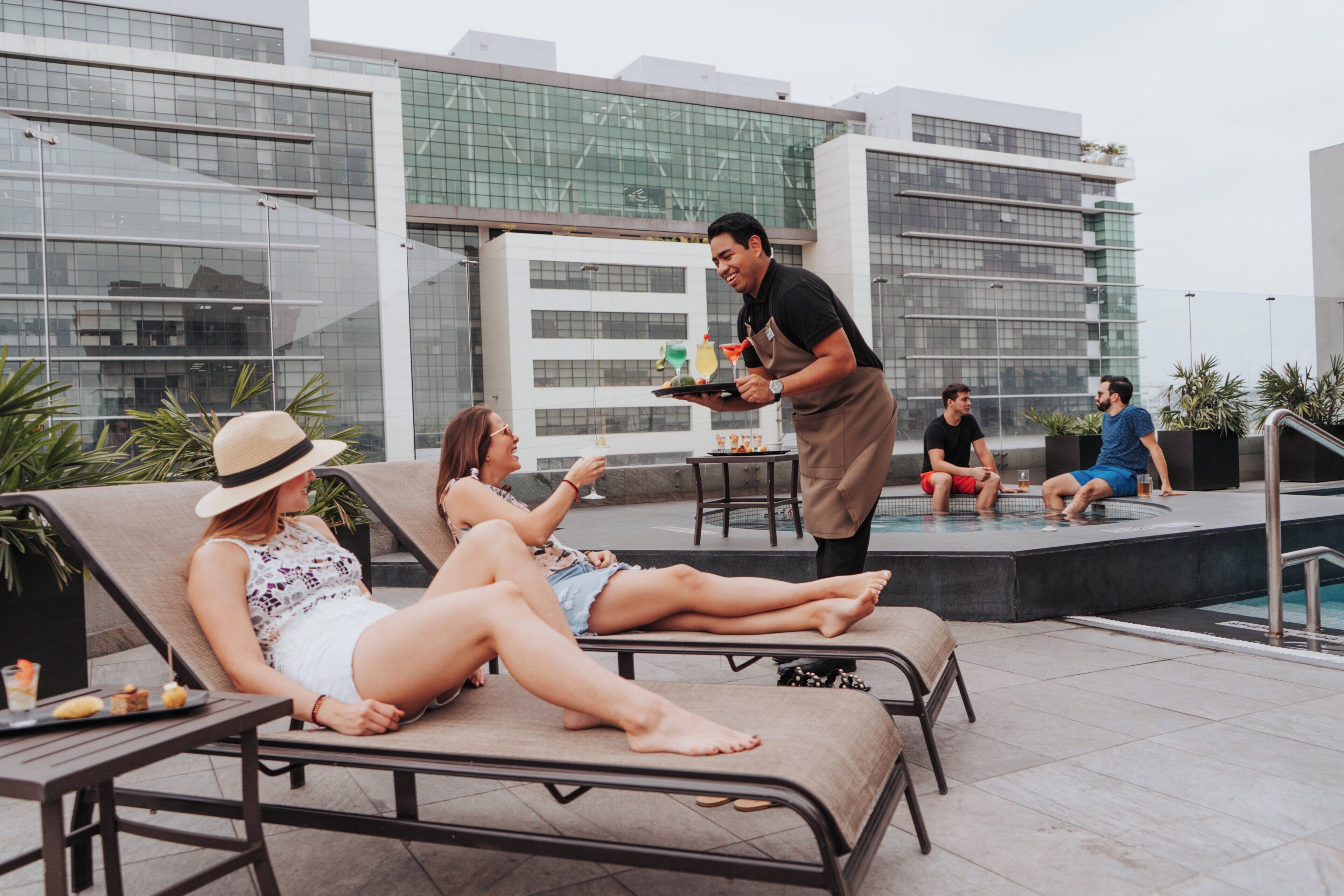 Un espace de détente aménagé sur le toit, avec des chaises longues, une piscine et un barman qui prépare des boissons.