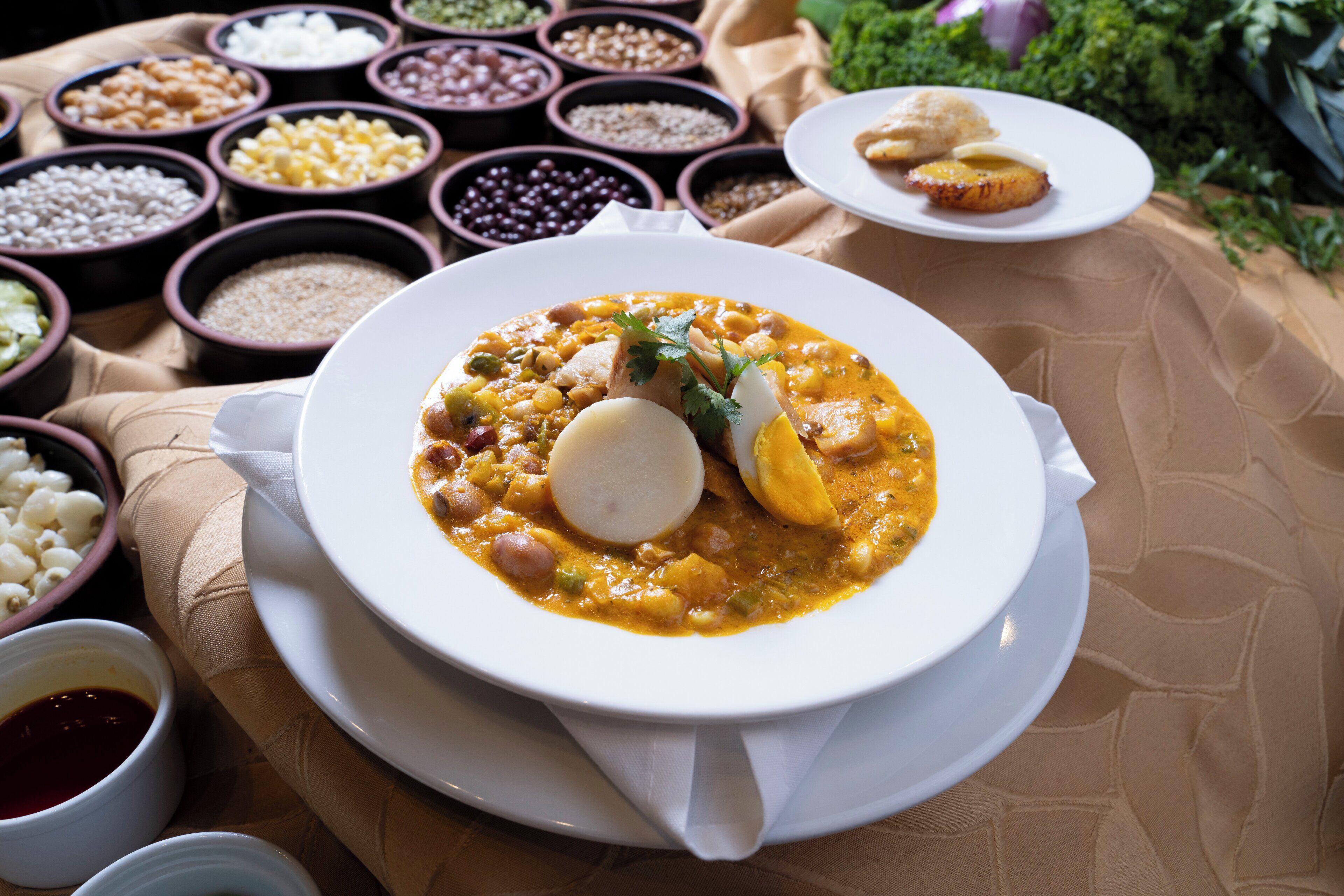 Una comida con un tazón de sopa y un plato de pan, rodeada de tazones con diversos granos y legumbres.