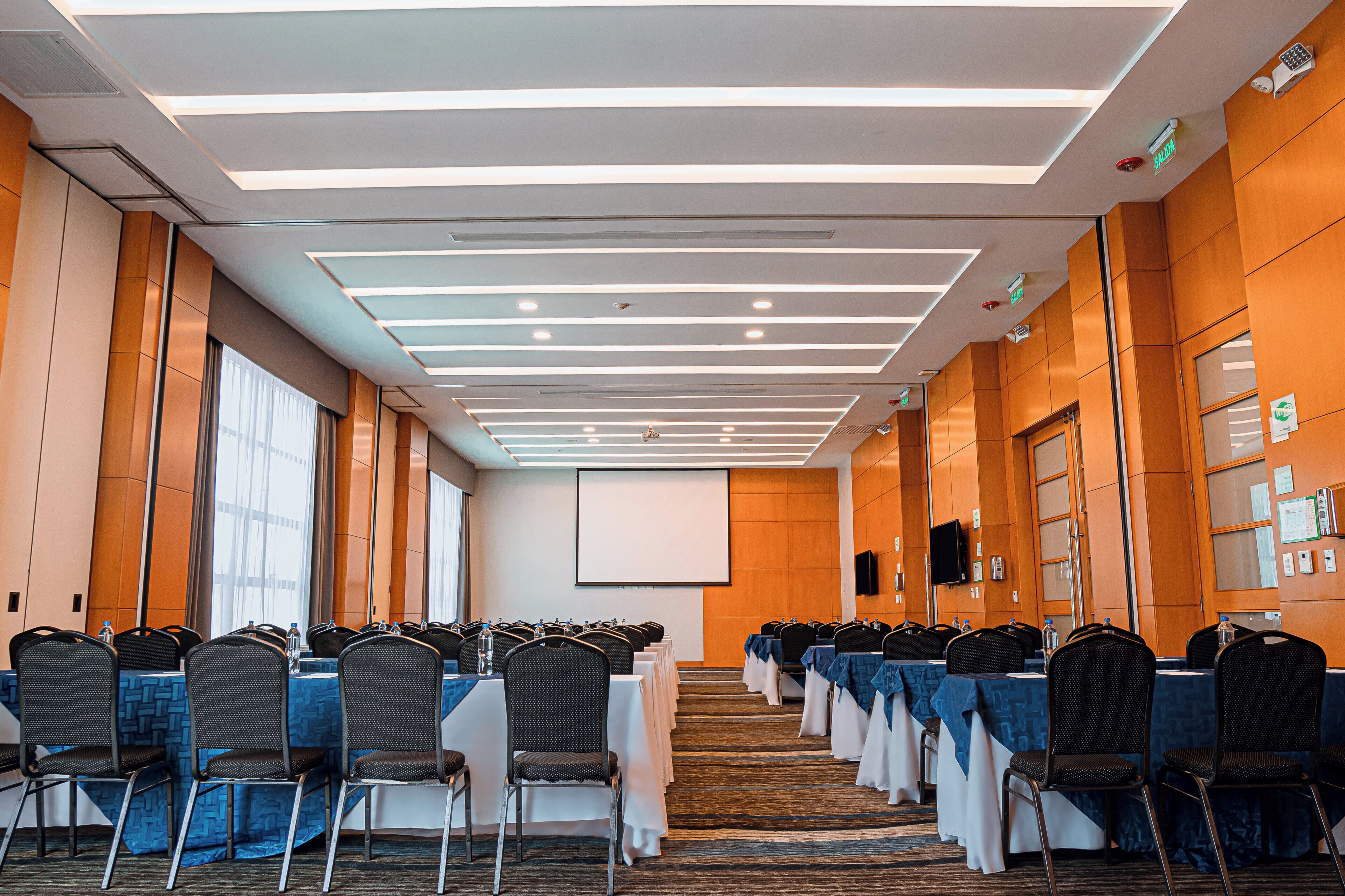 A conference room with rows of chairs, a projector screen, and a stage at the front.