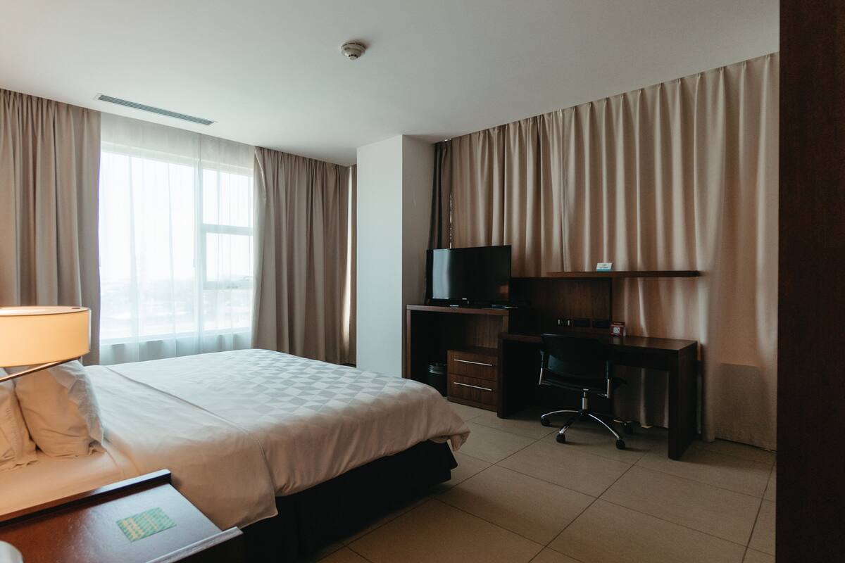 Een hotelkamer met een bed, een bureau met lamp, een televisie en een bureau met lades.