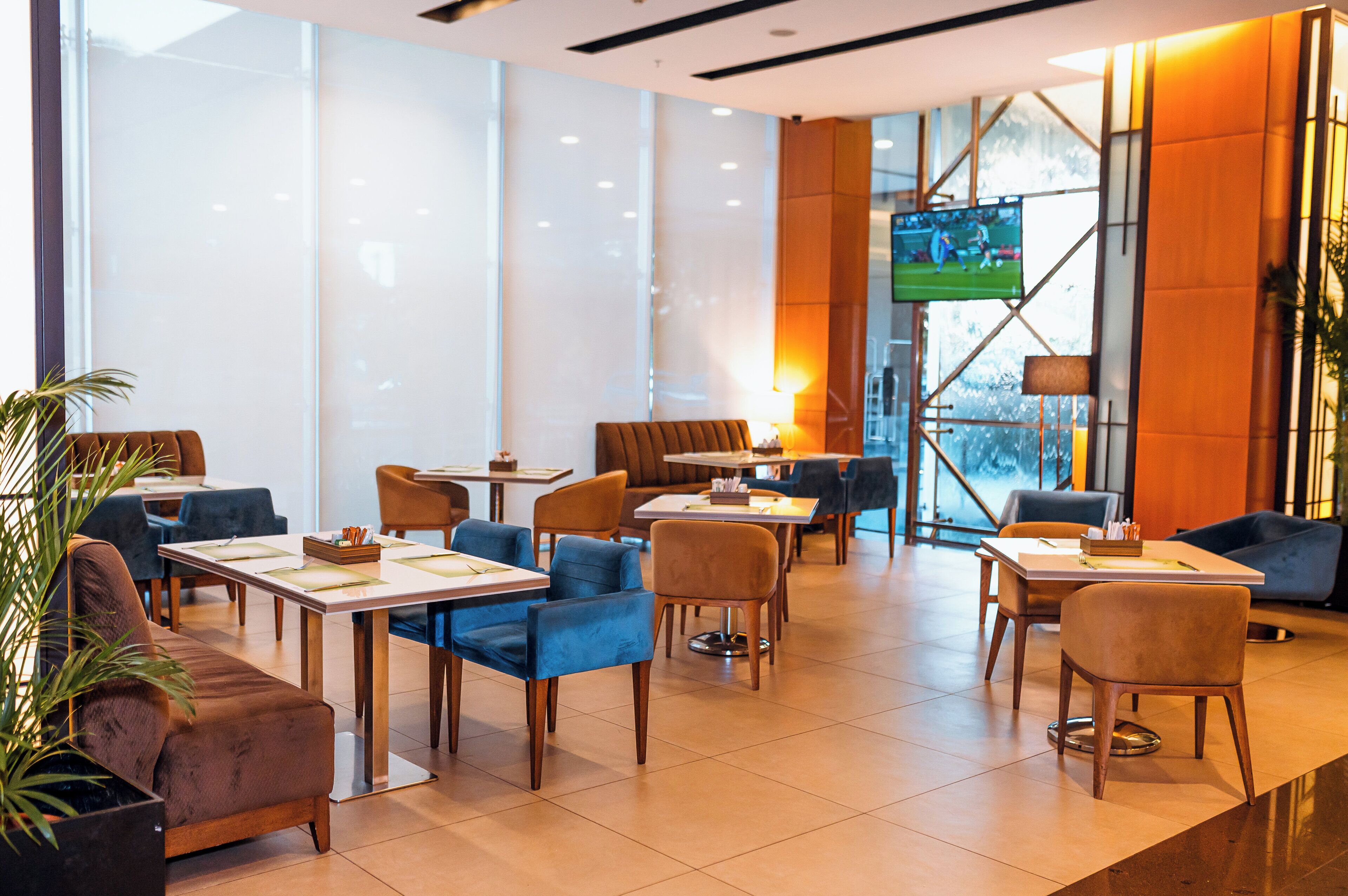 A hotel lobby with seating areas, tables, and a television screen.