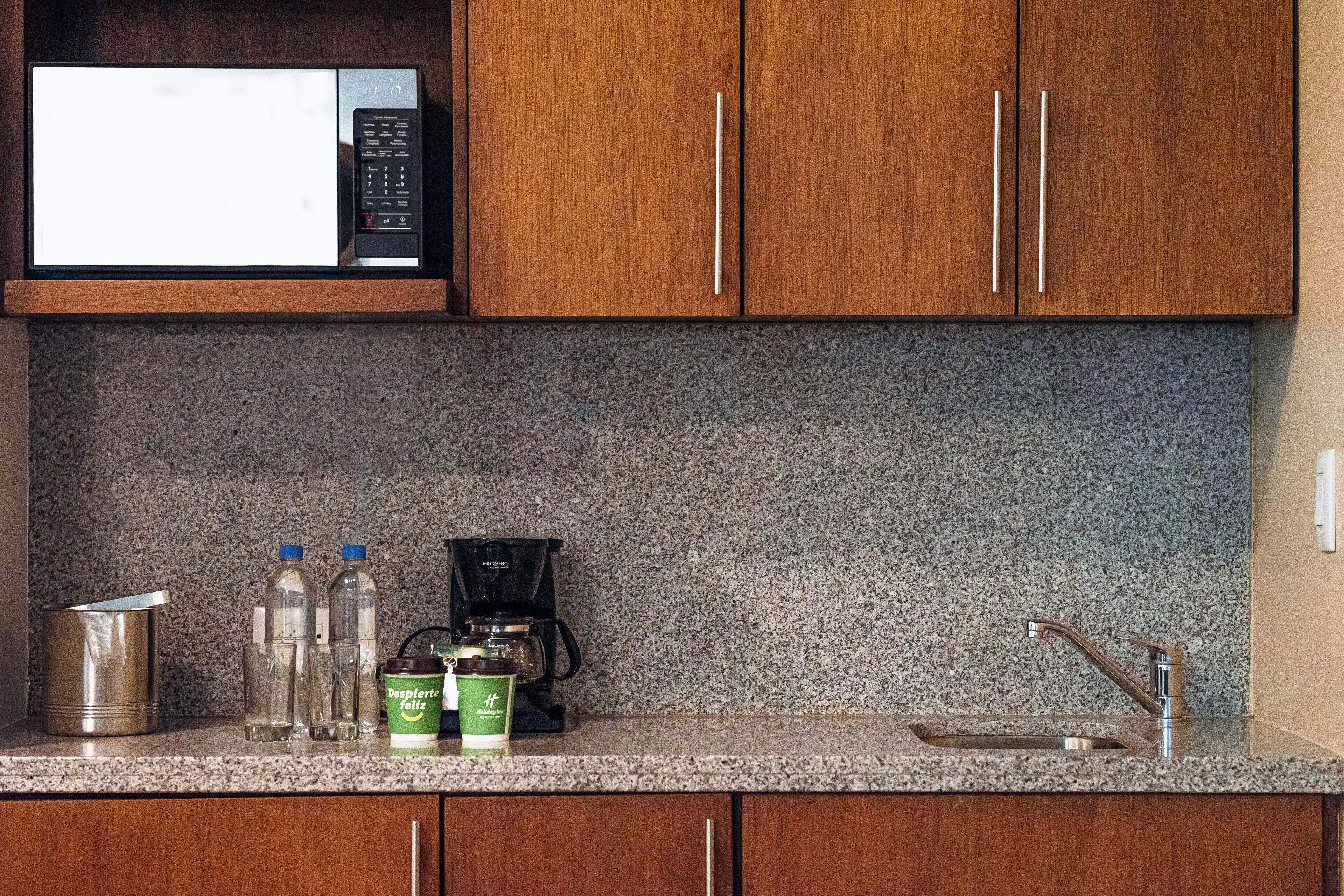 Una cocina con microondas, cafetera y un recipiente de acero inoxidable.