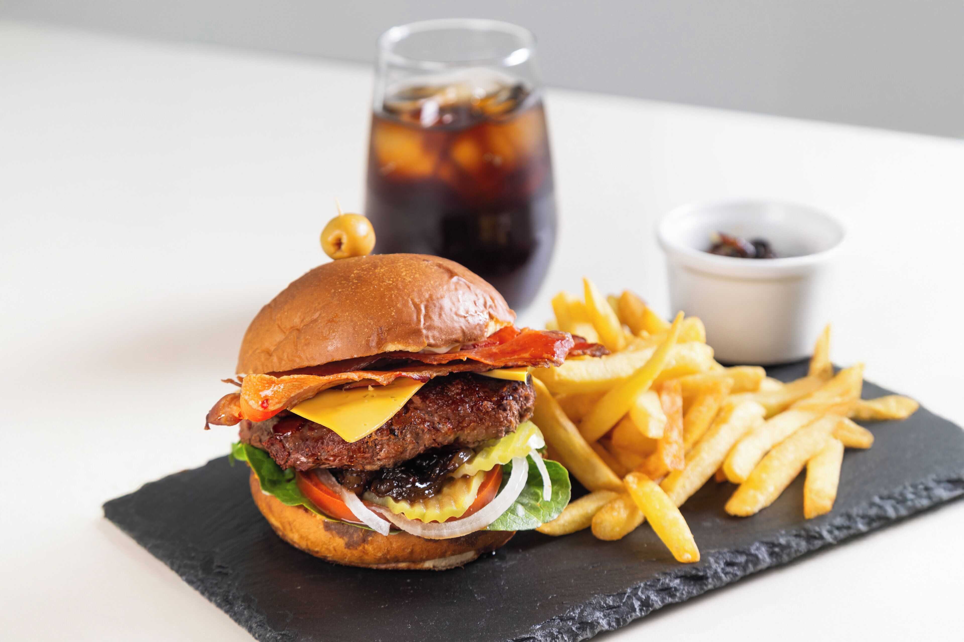 A burger with fries and a drink on a black slate plate.