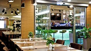 A restaurant interior with multiple dining tables, chairs, and a bar area visible through a glass partition.