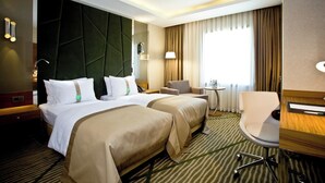 A hotel room with two beds, a desk, a chair, and a window with curtains. - Holiday Inn Gaziantep - Sehitkamil by IHG (Gaziantep)